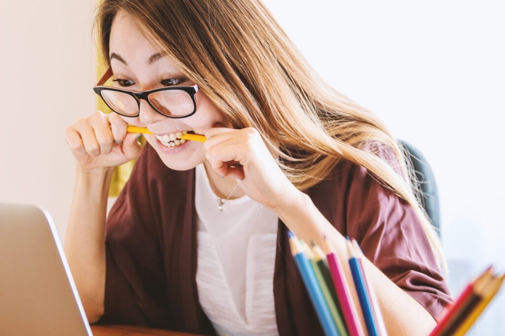 woman anxiously biting pencil in front of laptop