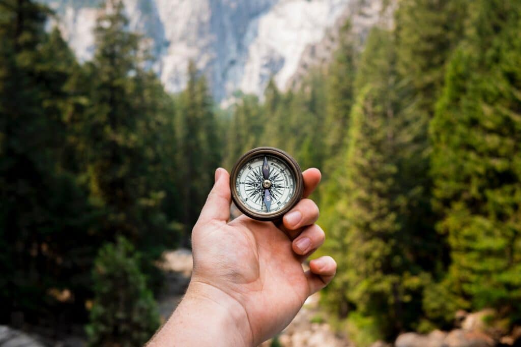 arms holding compass in front of camera with mountains in the background